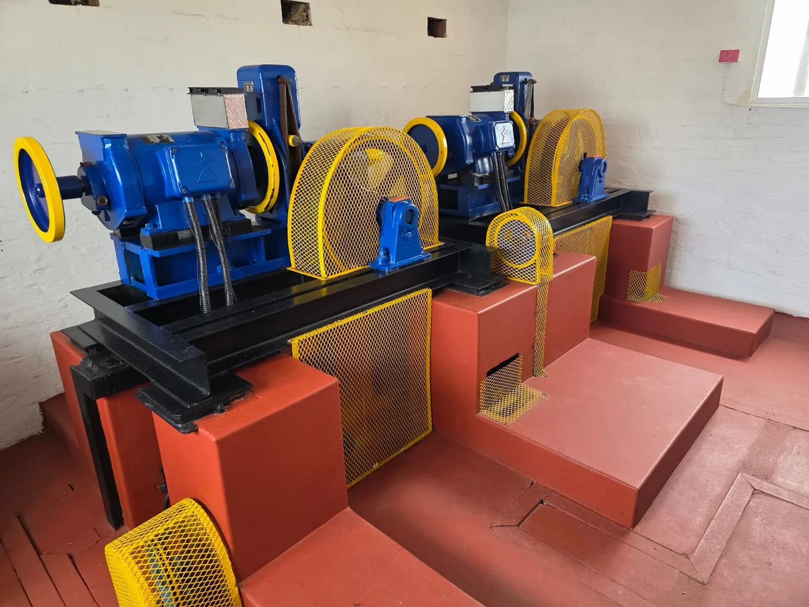 Blue lift machinery with yellow protective guards in a machine room.